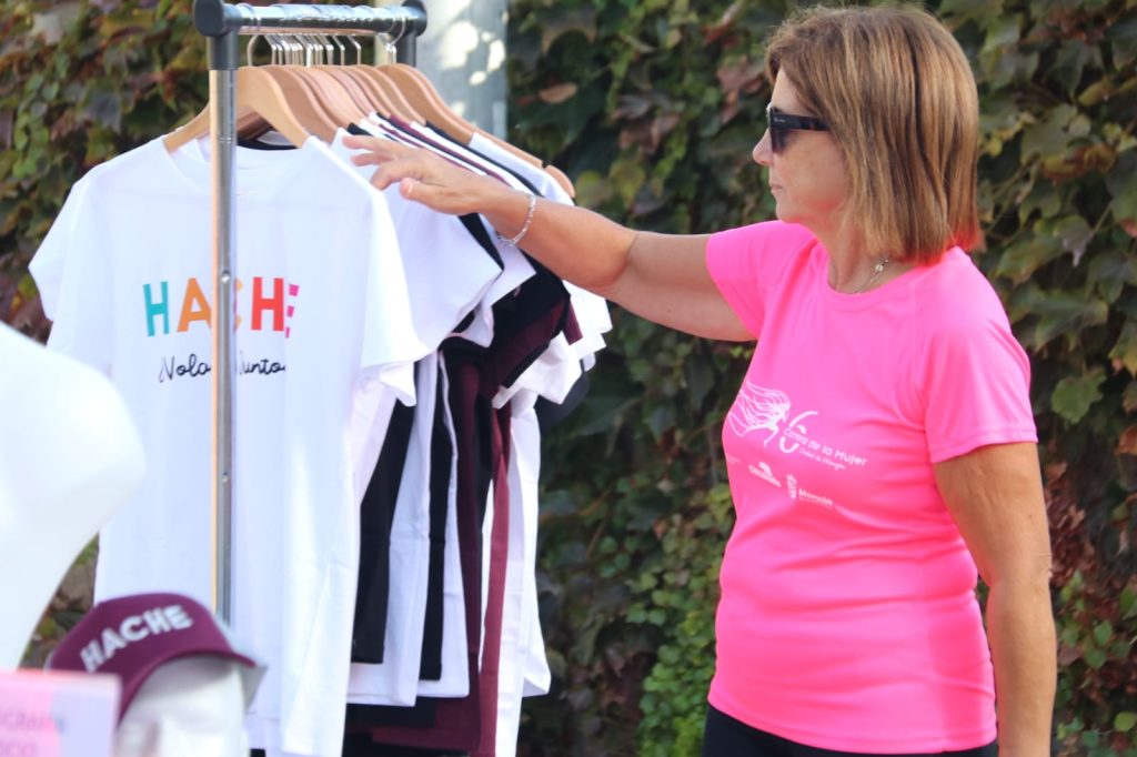 Una mujer con camiseta de la carrera mueve las perchas del burro mirando las camisetas Hache que están colgadas