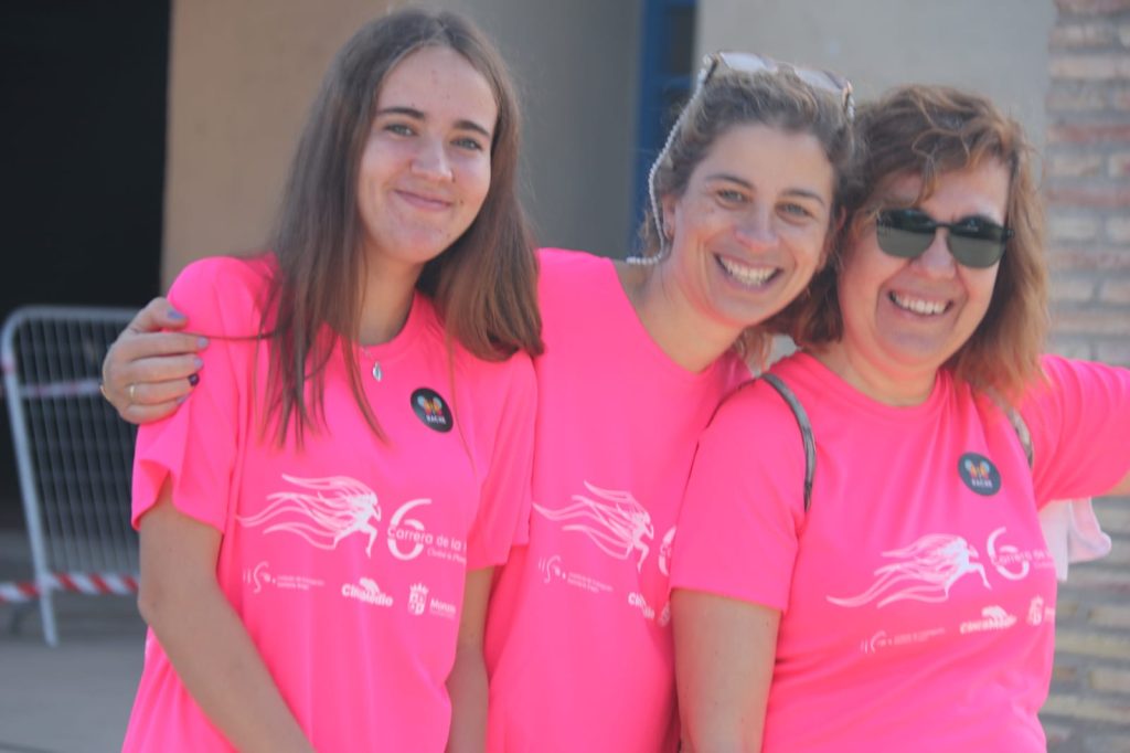 3 chicas, familias de AMO en primer plano vistiendo la camiseta de la carrera, abrazadas