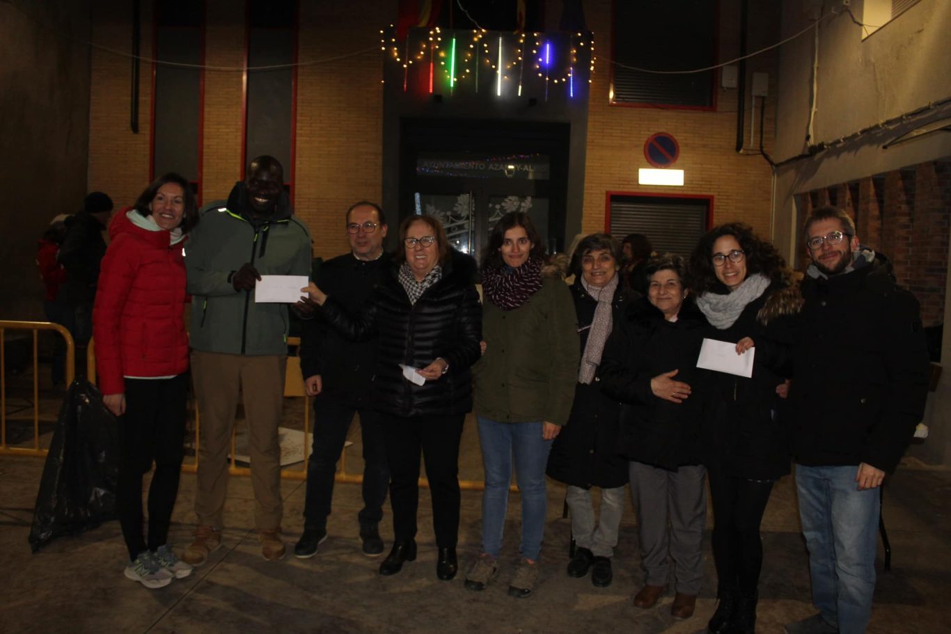 Grupo de personas posan en fila enseñando los cheques del importe recibido en la merienda solidaria de Azanuy