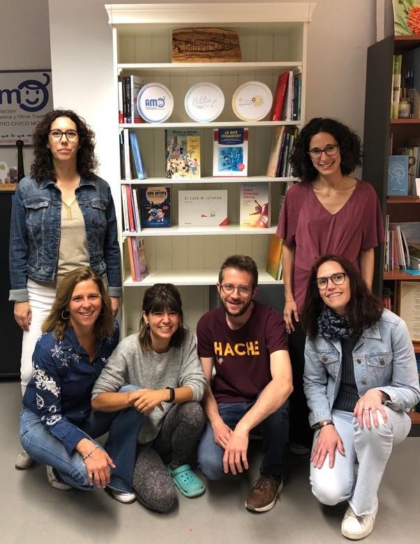 3 personas del equipo AMO y 3 de la fundación Quality Corn posan delante de la librería con los ejemplares de la BiblioTEA