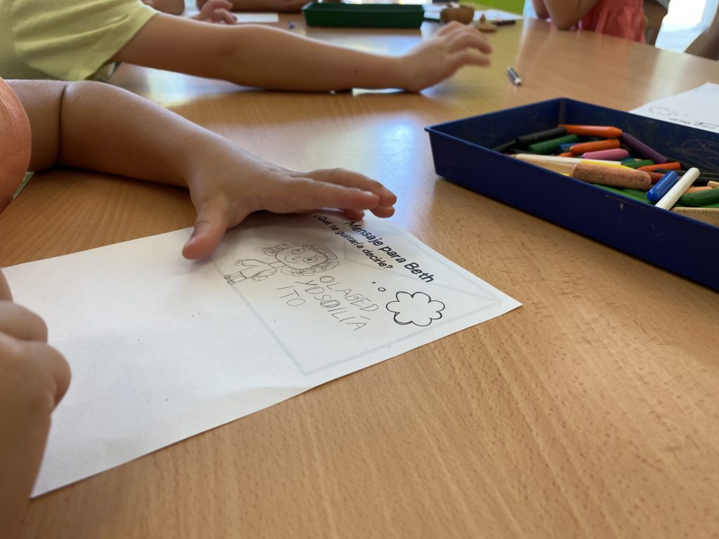 En un primer plano, las manos de un niño dibujando a Bet en una hoja